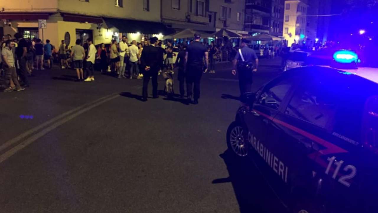 Folla di persone riunite davanti a un bar con in primo piano dei carabinieri