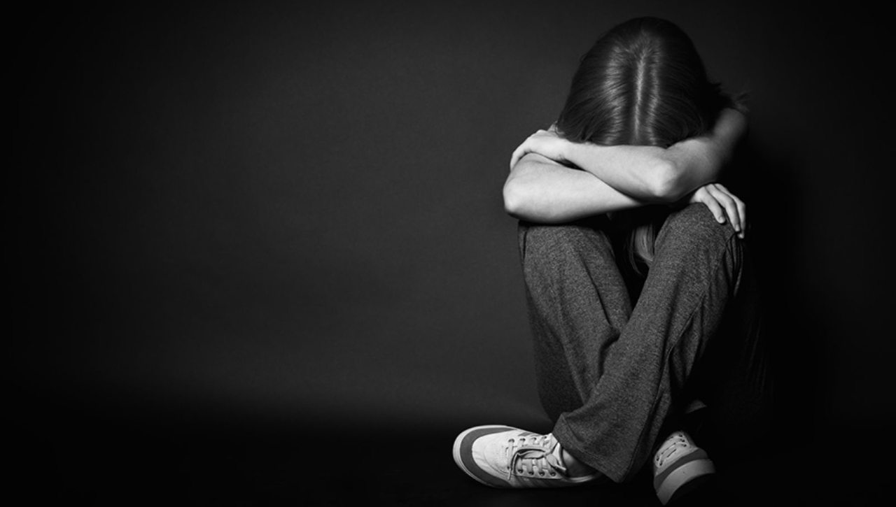 Depressione, ragazza piegata su se stessa su sfondo bianco e nero