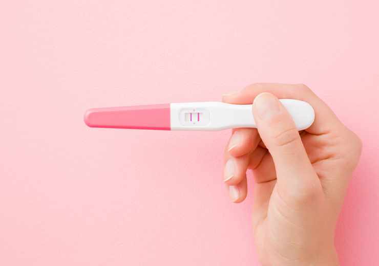 Test di gravidanza tra mani femminili, sfondo rosa