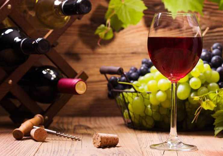 calice di vino in primo piano con bottiglie di vino rosso e uva in un cesto in secondo piano