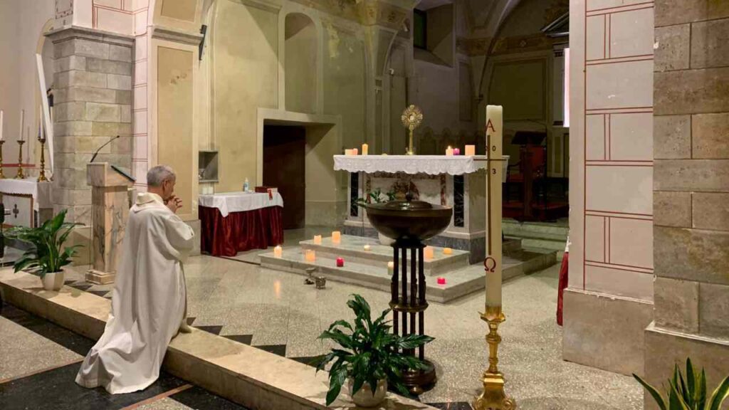 Sacerdote in ginocchio a mani giunte sull'altare